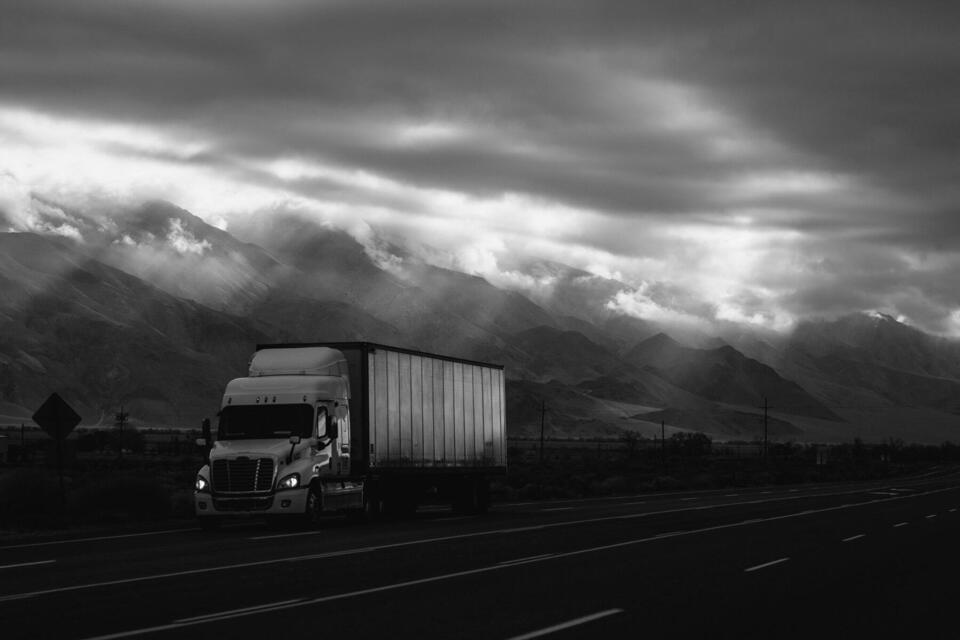 Freightliner Cascadia with dry van trailer beneath mountain storm clouds